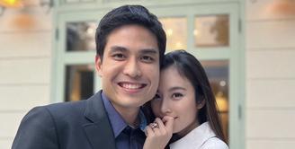 Nong Poy memamerkan cincin saat bersama calon suaminya. Dalam foto tersebut, ia mengenakan coat abu-abu dengan riasan wajah minimalis bahkan terlihat tanpa makeup. @poydtreechada.